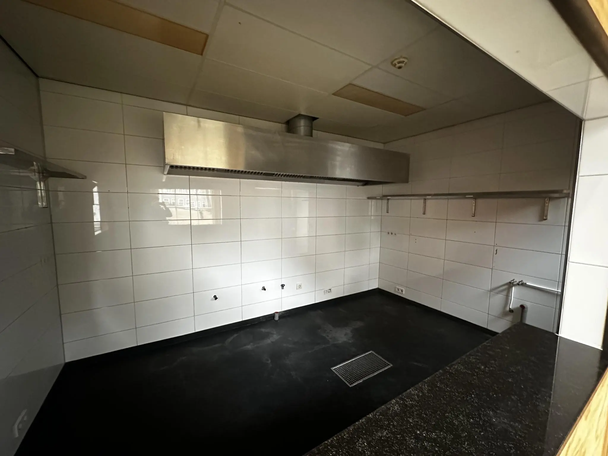 Lege horecakeuken met witte tegelwanden, een zwarte vloer en een grote roestvrijstalen afzuigkap aan het Sint-Agathaplein.